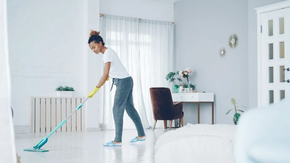 A woman carefully wraps a sofa in protective material while packing boxes in a bright room.